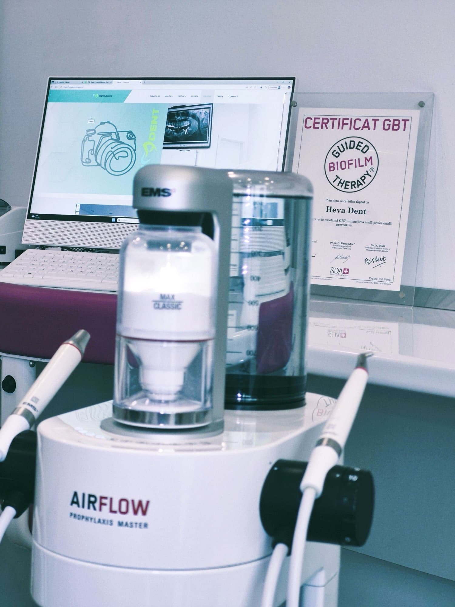 The EMS Airflow Prophylaxis Master unit, with its two handpieces, in one of the clinic's treatment rooms; behind it, the clinic's framed GBT certificate